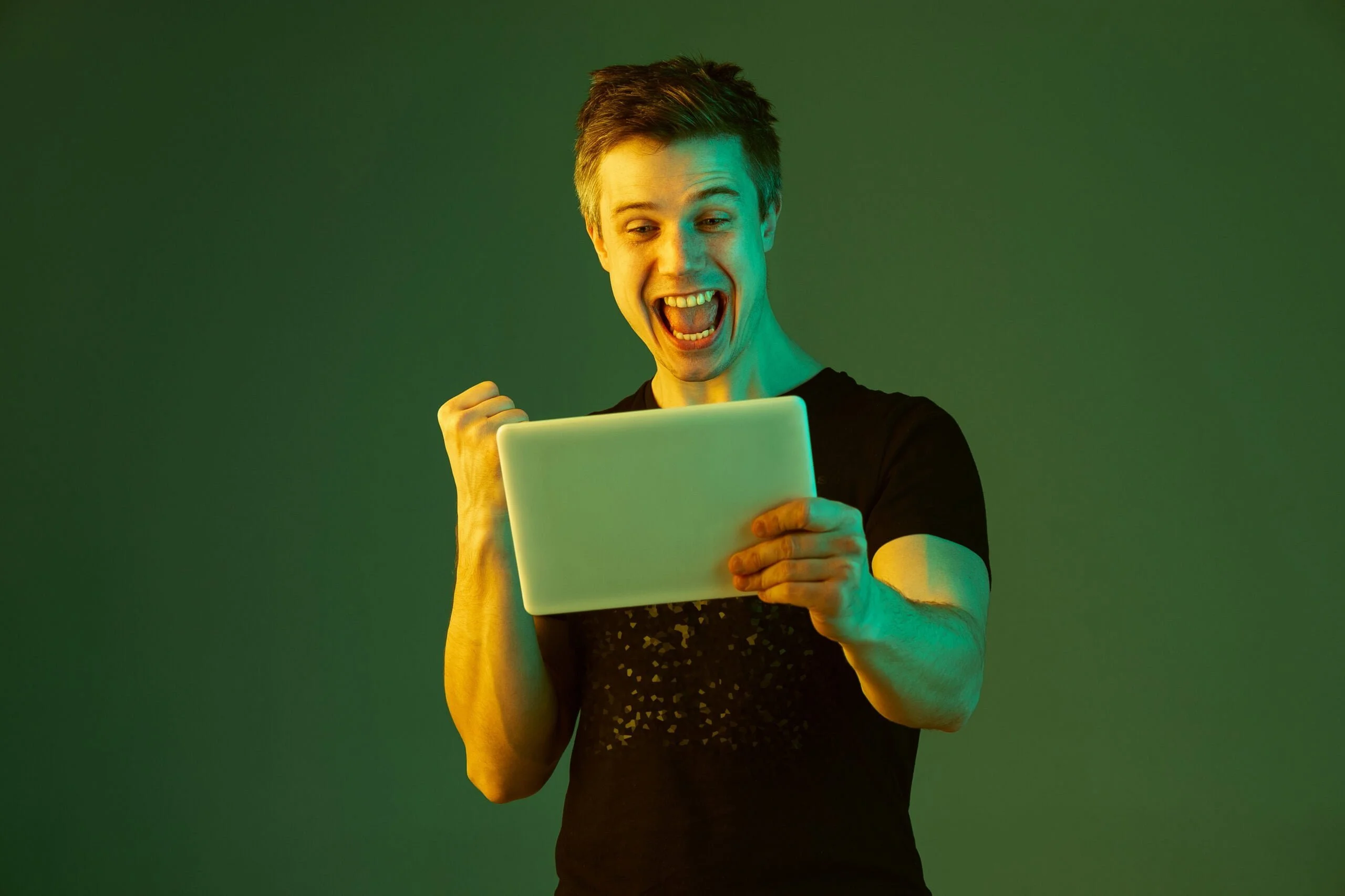 Choosing Online Casinos: Comparison Of Online Casino Payout Policies in Different Countries and Regions 1 holding tablet celebrating win bet game caucasian man s portrait green studio background neon light beautiful male model concept human emotions facial expression sales ad scaled 1